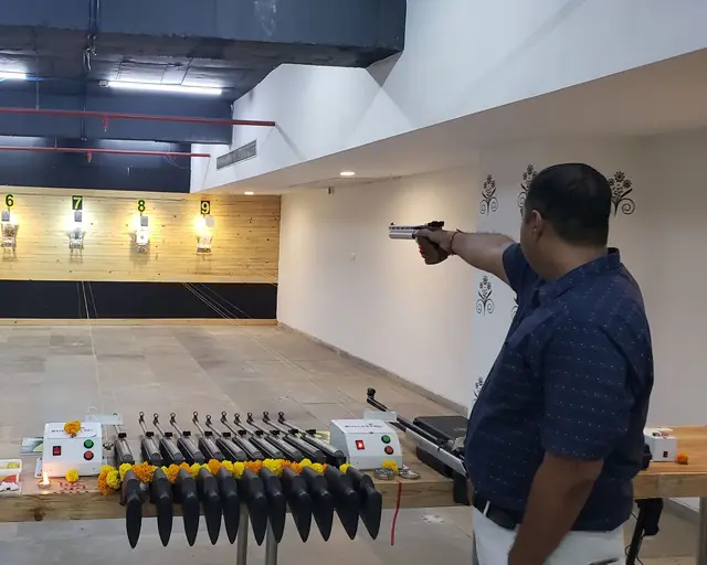 A pistol shooter on the 10m air pistol line, pistols racked in the foreground